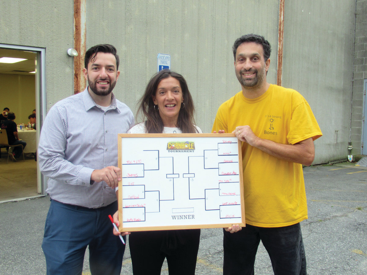 BRACKET BOARD: Keri Salinger, center, holds the official bracket board for the Cornhole Elimination Tournament. She is joined by her son Justin Salinger, left, and committee member Mark Berger.